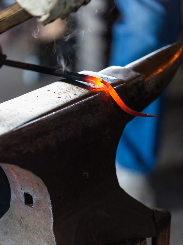 blacksmith bending hot iron on the anvil.